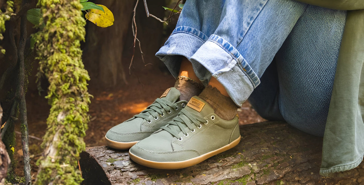 A lady sitting on a log of wood wearing the FREESTYLE 3 Pine, Barefoot Shoes from Splay. 