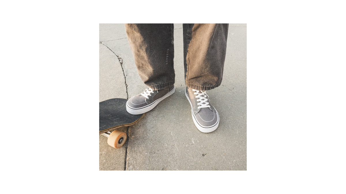 A man wearing Splay Shoes REV HT London standing with a skateboard.  