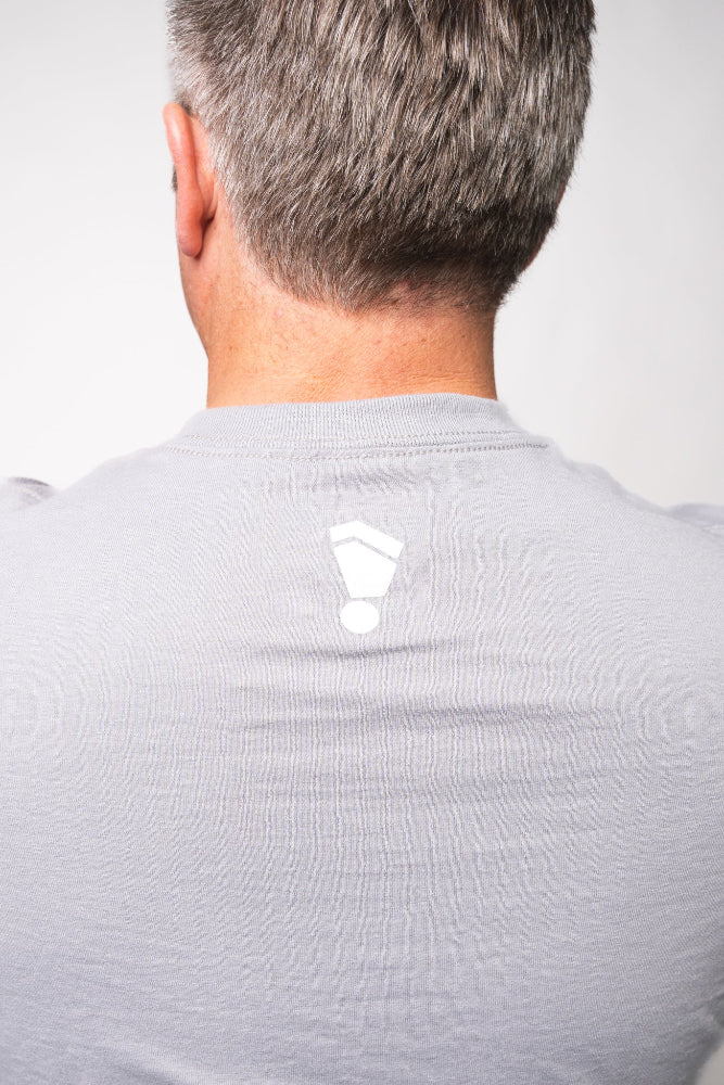 Back view of a person wearing a light gray shirt with a logo on a white background